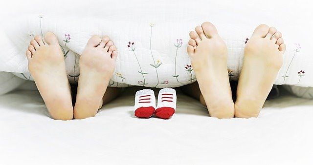 夫婦の足の裏の間に、子供用の靴下が置かれた写真です。